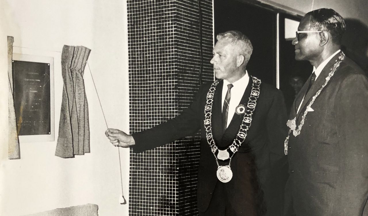 Two men with their mayoral chains on unveil a plaque on a white wall.