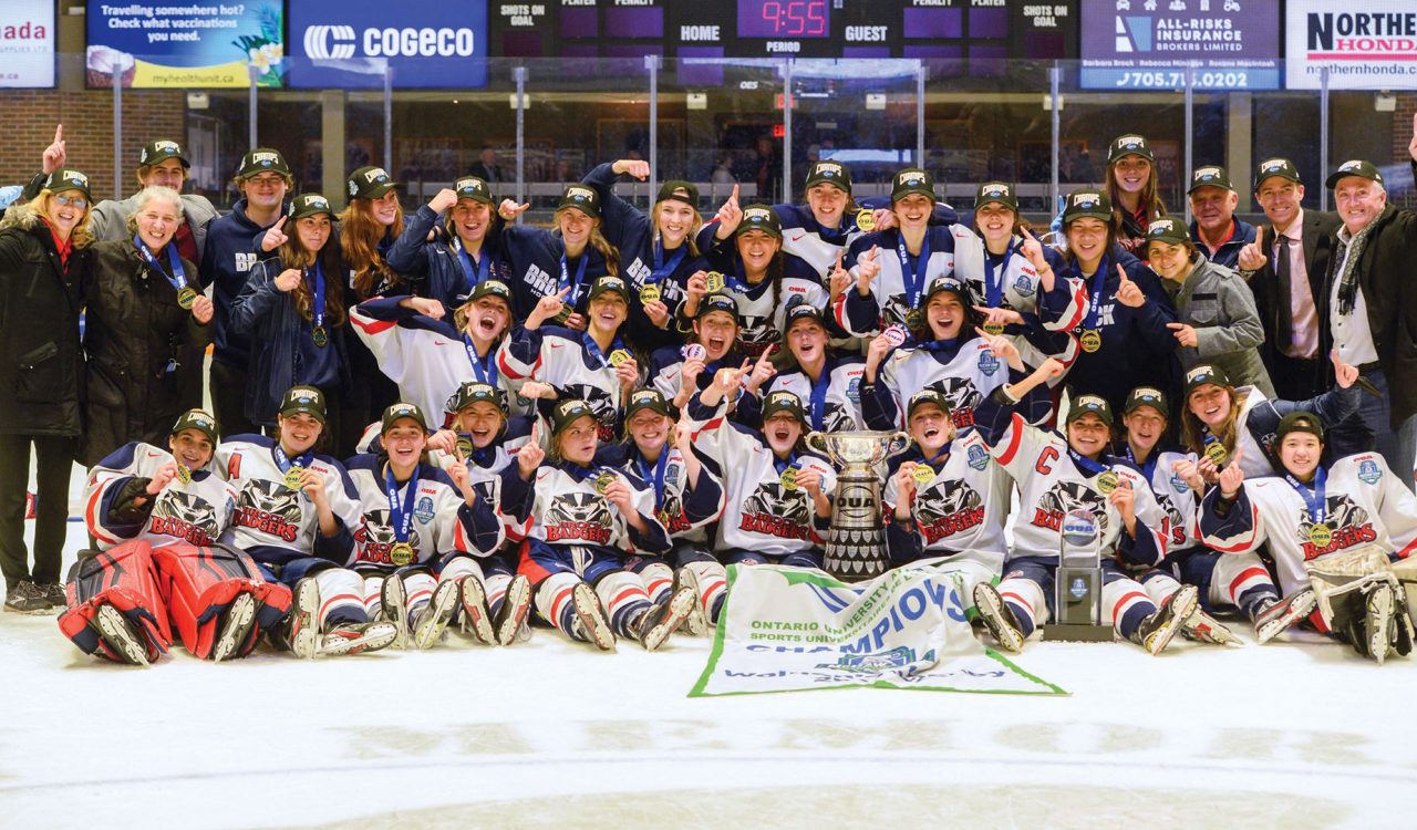 A women’s hockey team poses with the championship trophy on ice.