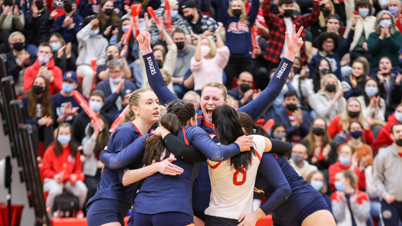 Women’s volleyball players celebrate in front of a crowd-filled gym.
