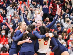 Women’s volleyball players celebrate in front of a crowd-filled gym.