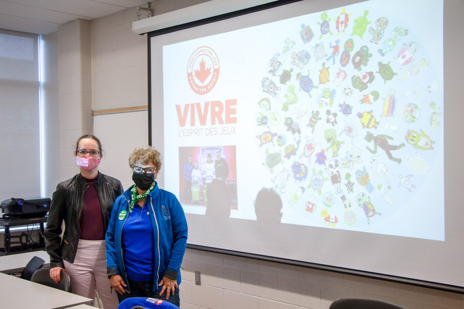 Two women stand in front of a screen showing proposed designs for the Niagara 2022 Canada Games mascot, Shelly.