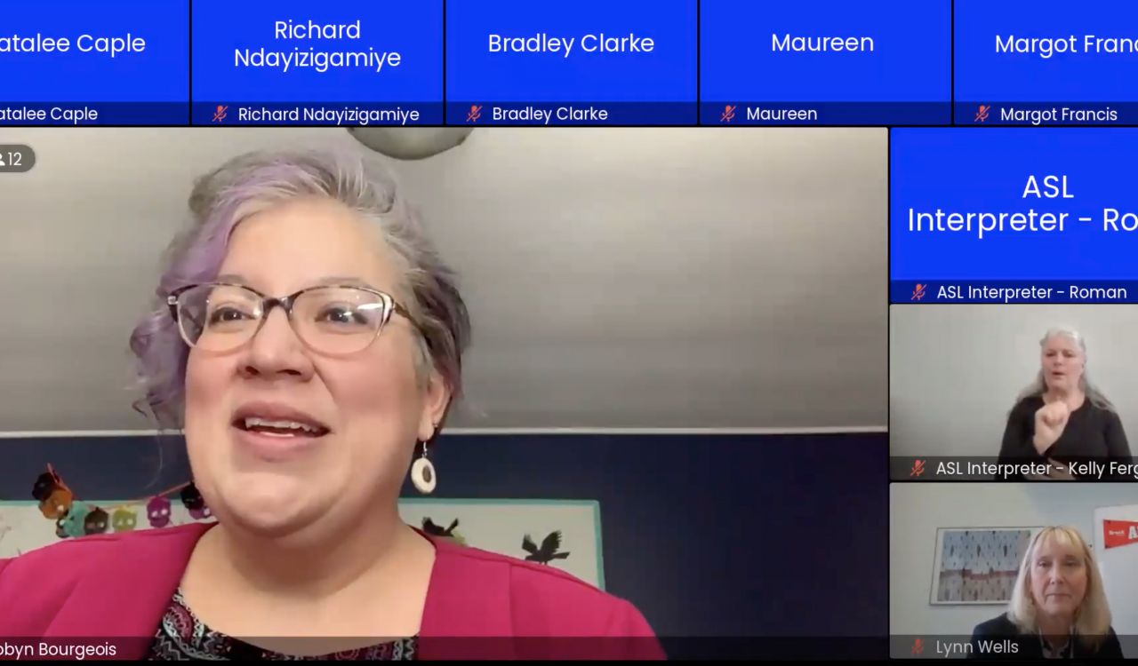 A screenshot of participants in an online meeting. A large box in the centre shows a woman speaking. Several blue boxes around the woman represent other people who will be presenting at the meeting. Their video cameras are off so all that is seen is their name written in text. Two of the small boxes show the faces of two other women.