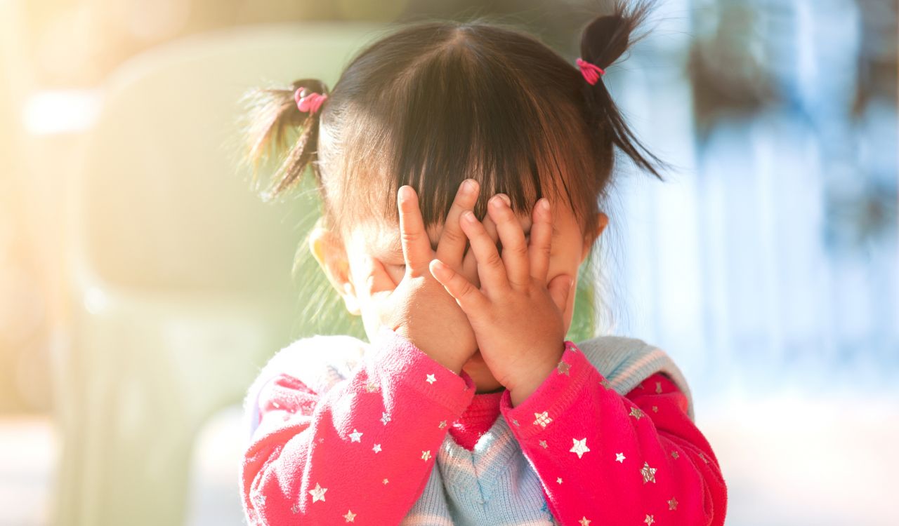 A small child covers her face with her hands.