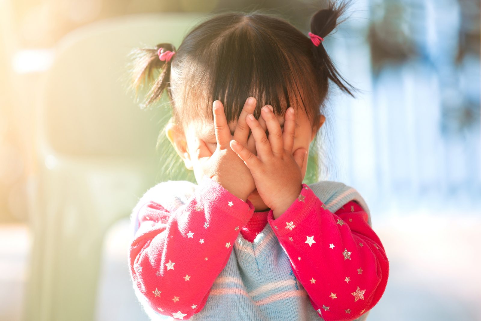 A small child covers her face with her hands.