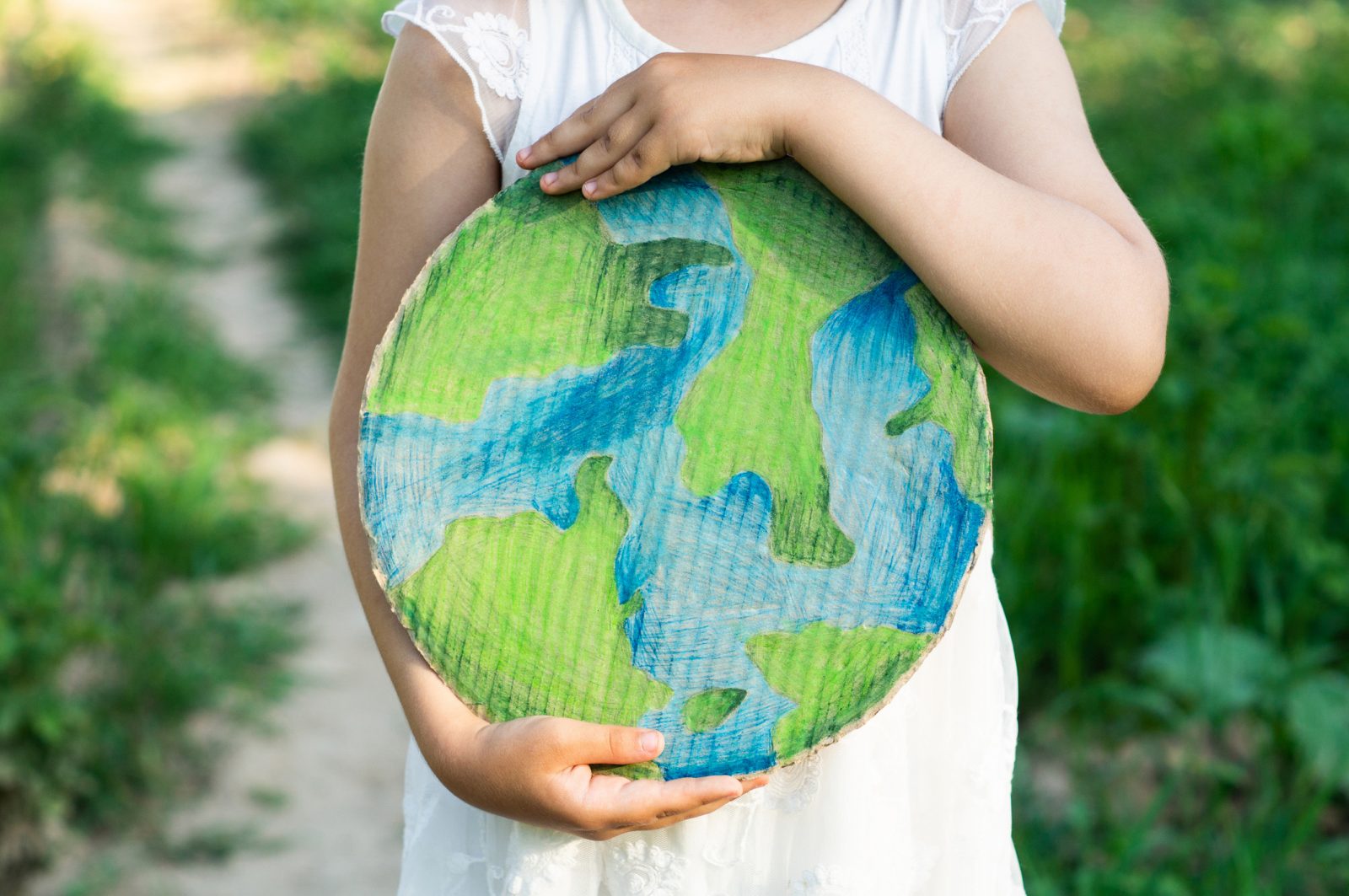 A child standing on an outdoor path and holding a cardboard circle painted to look like Earth.