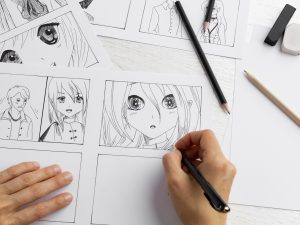 An illustrator’s hands drawing anime-style characters in black ink on white paper, with drawing tools scattered on the desk.
