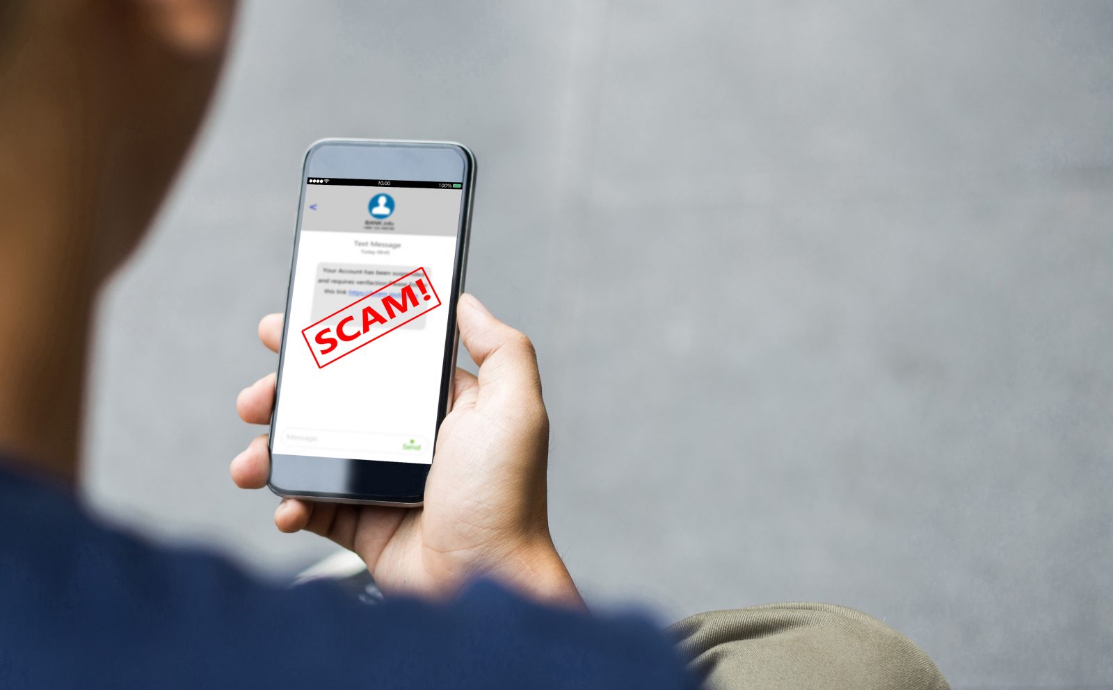A man holds a smartphone with the word "Scam!" written across the screen in bold red letters.