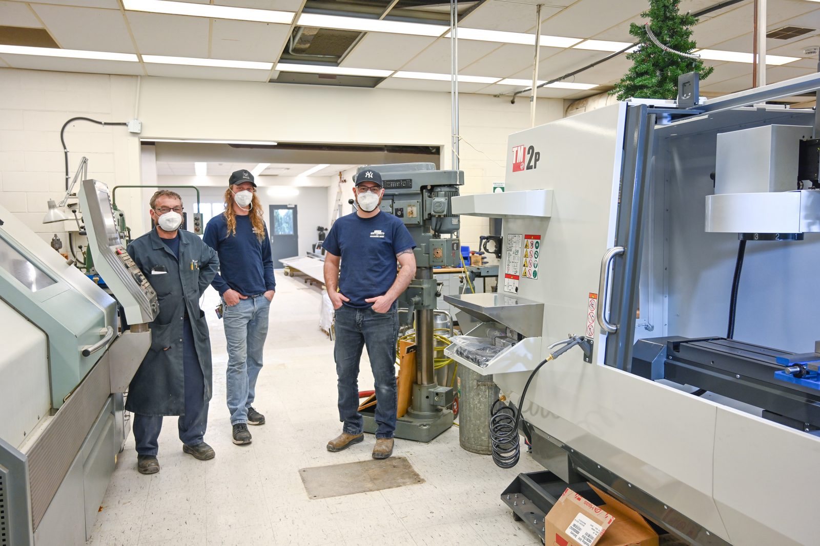 Three staff members stand among shop tools and machines in Brock University’s Machine Shop.