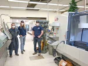 Three staff members stand among shop tools and machines in Brock University’s Machine Shop.