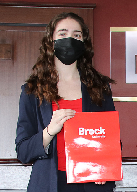 A young woman holds a red folder with ‘Brock University’ written in white near the top.