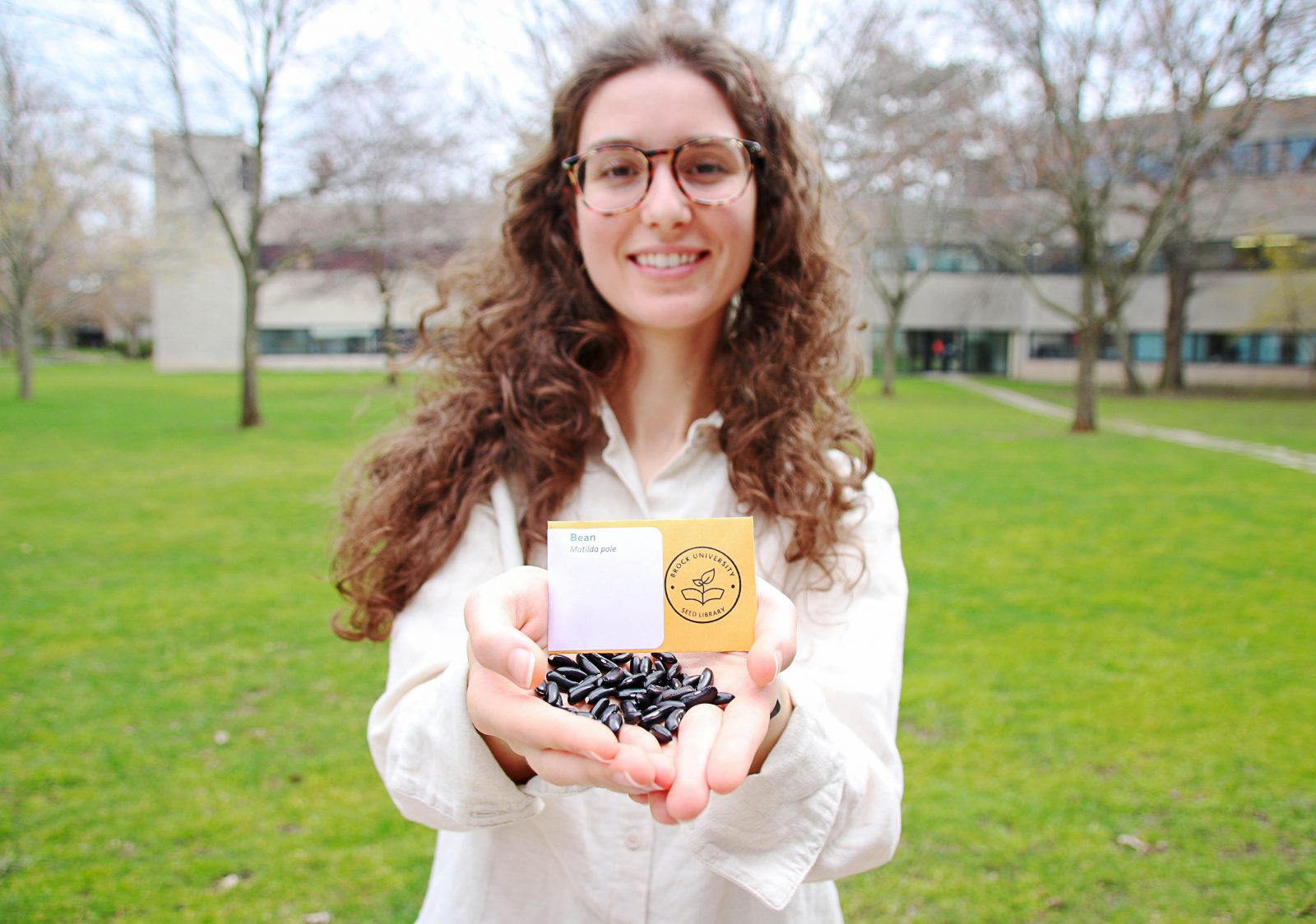 A woman holds dried black beans and a card for the Brock University seed library.
