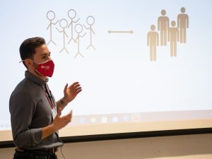 Male university student standing next to screen showing his PowerPoint presentation.