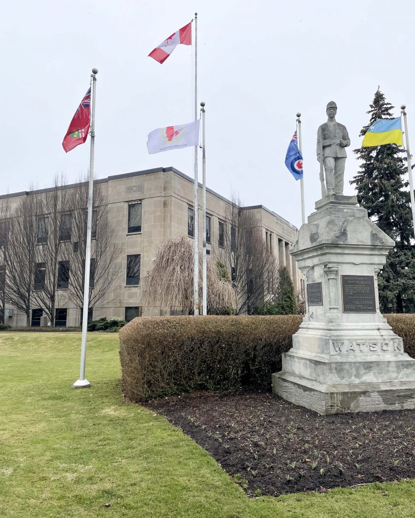 A photo of flags flying on flagpoles in front of a brown building.