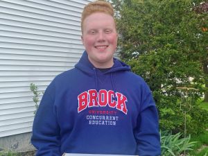 A young man in a blue Brock University hoodie holds a box that says congratulations on it.