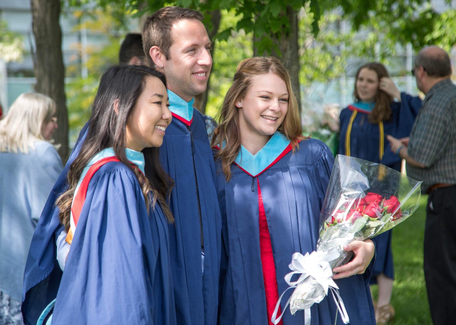 Three graduates stand together posing for a photo outdoors.