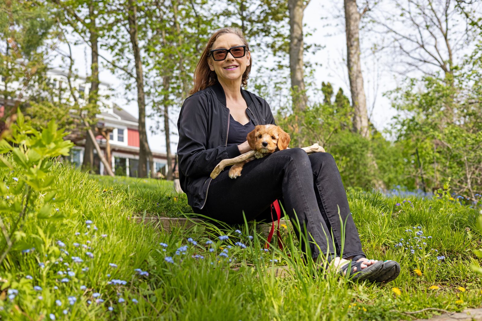 Brock Associate Professor of Visual Arts Donna Szoke sits on a grassy hill with a small brown puppy in her arms.