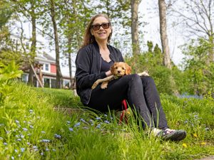 Brock Associate Professor of Visual Arts Donna Szoke sits on a grassy hill with a small brown puppy in her arms.