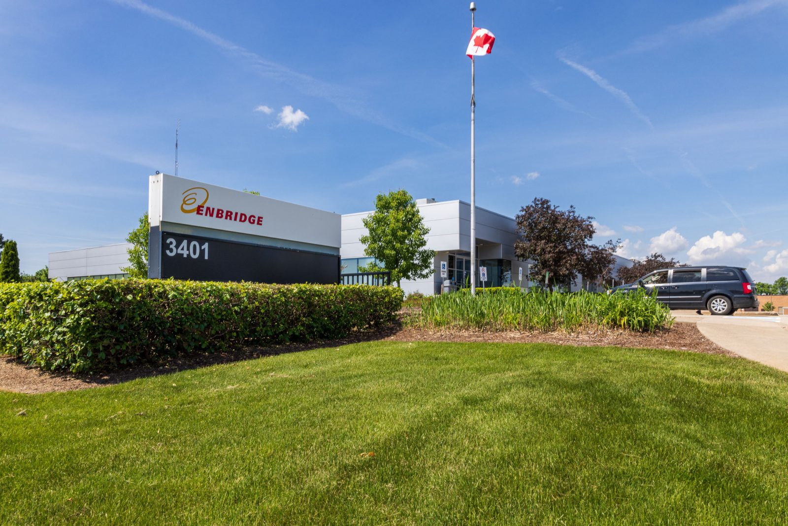 A building with an Enbridge sign with green grass in the foreground and blue sky above.