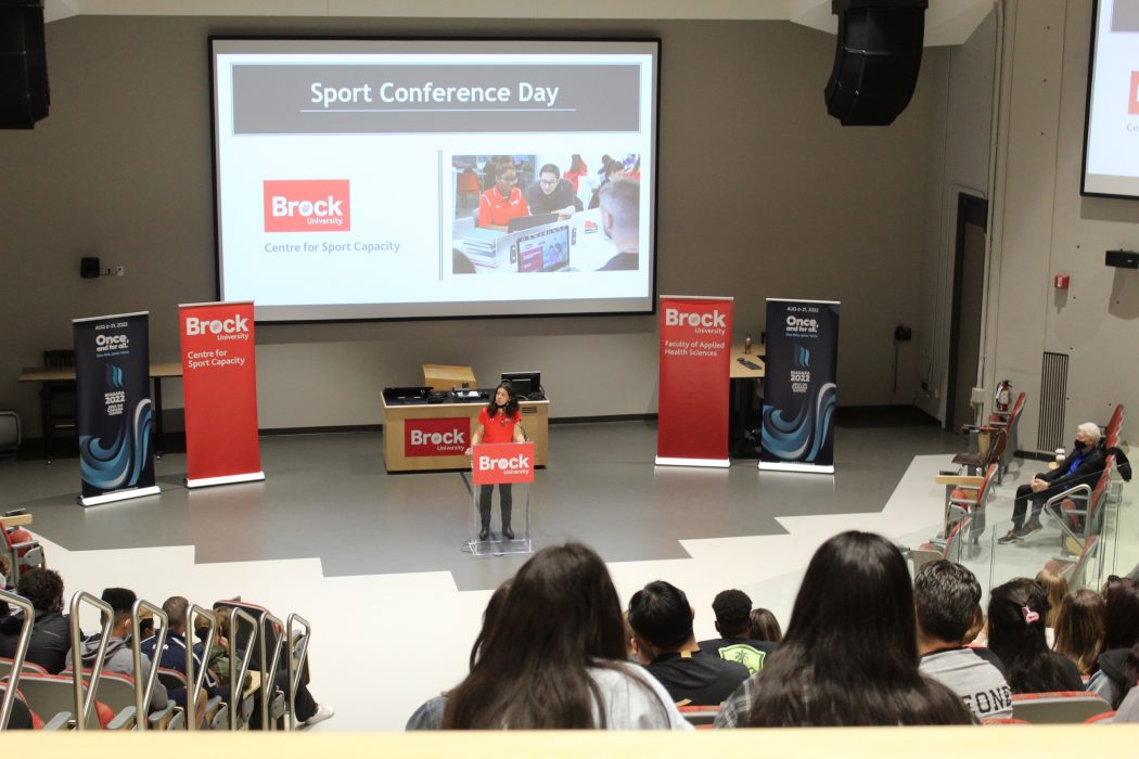 A woman speaks at a lectern in a lecture hall filled with people.