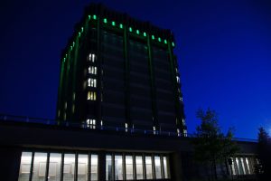 A large concrete 13-storey building with green lights cascading down each side.