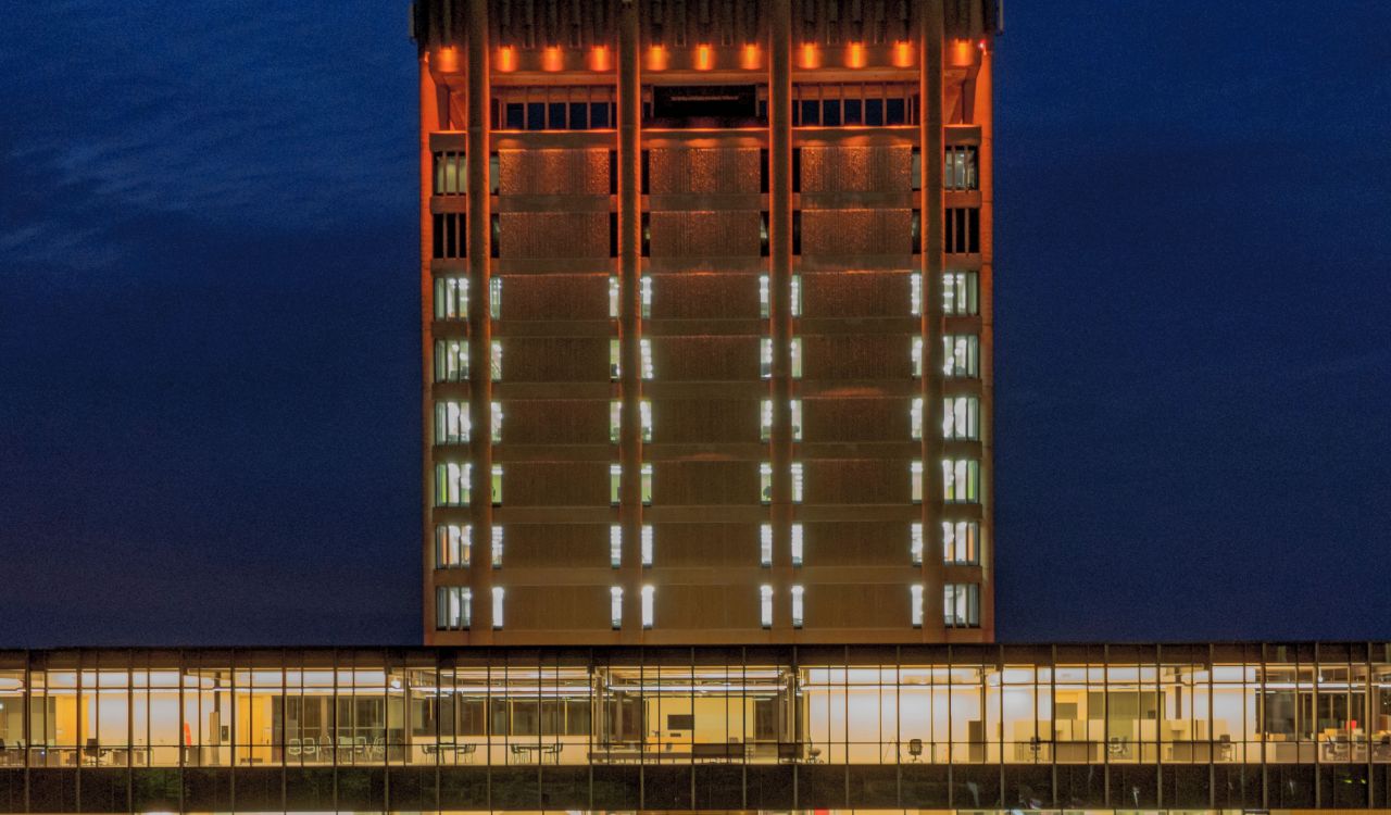 Brock University’s Arthur Schmon Tower lit in orange LED lights. In front of the 13-floor tower is the glass-walled Rankin Family Pavilion. A Campus Security Services vehicle is parked in front of the buildings. In the foreground is a bronze statue of Maj.-Gen. Sir Isaac Brock, the University’s namesake.