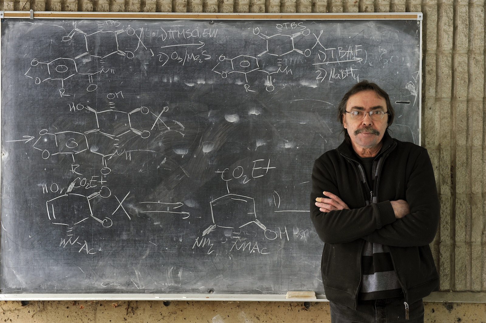 Brock Chemistry Professor Tomáš Hudlický stands against a blackboard with formulas written on it in white chalk.
