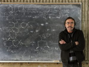 Brock Chemistry Professor Tomáš Hudlický stands against a blackboard with formulas written on it in white chalk.