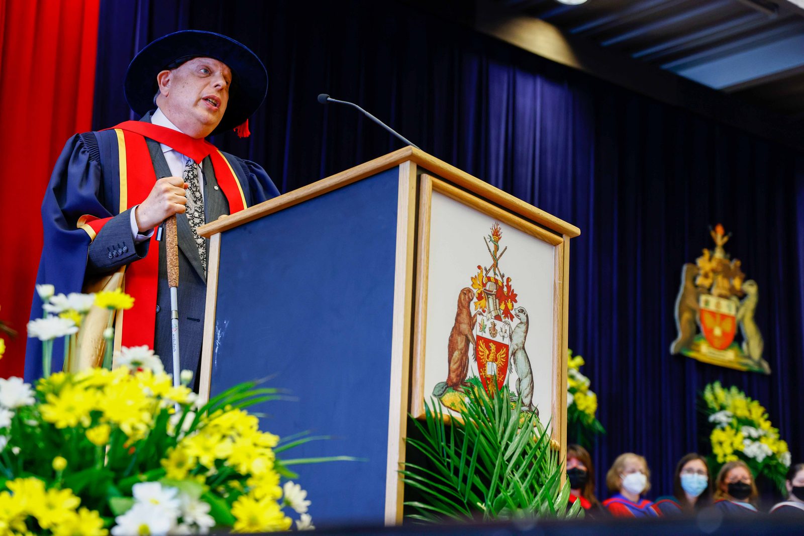 A man in a graduation gown stands at a podium.