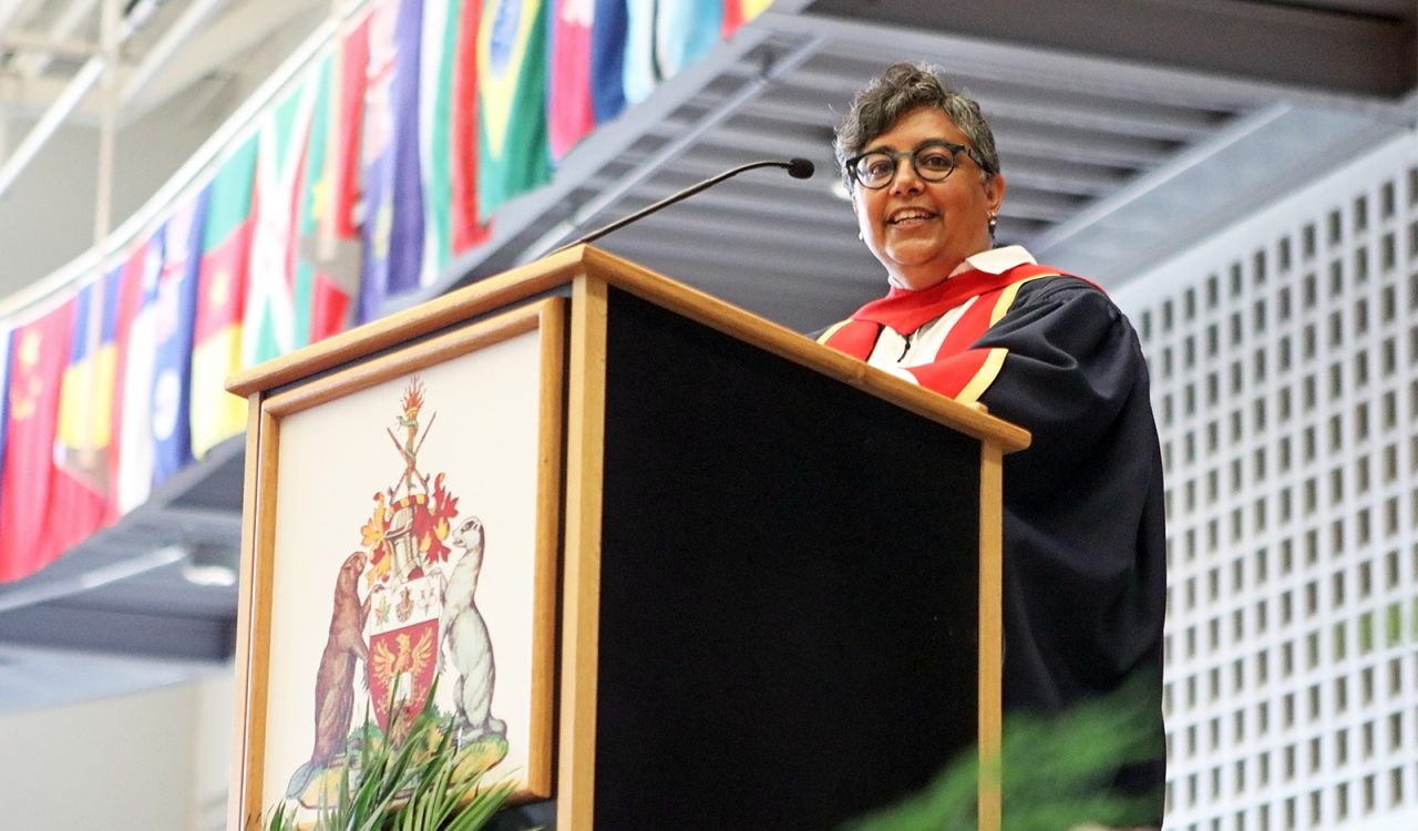 A woman in a graduation gown stands at a podium.