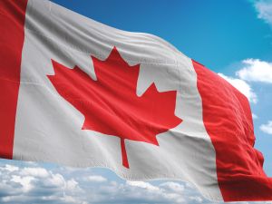The red and white Canadian flag waving against a blue sky and white clouds.