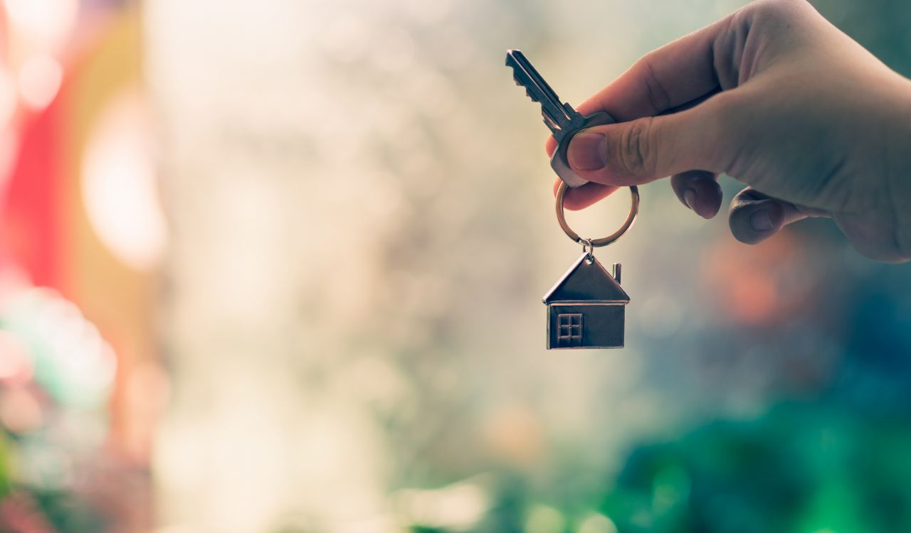 A hand holds up a key with a keychain of a small metal house.