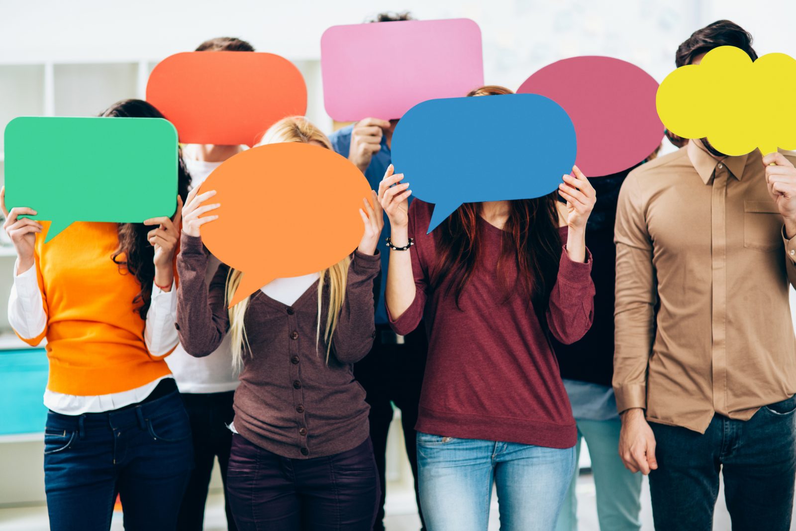 A group of seven youths hold coloured paper cut to resemble speech bubbles in front of their faces.