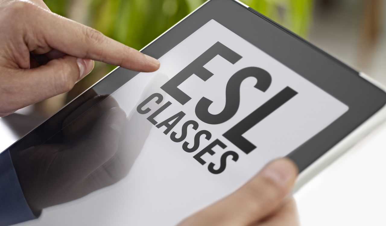 Hands hold a tablet with a screen that reads “ESL CLASSES” against a green background.