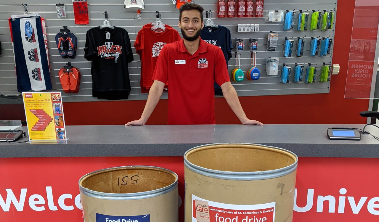 A smiling man stands behind a service desk with two large donation bins in front of the desk.