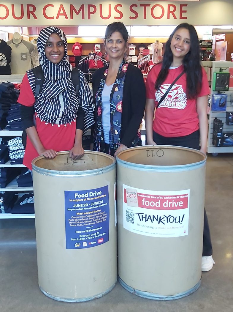 Three women stand behind two large food donation bins.