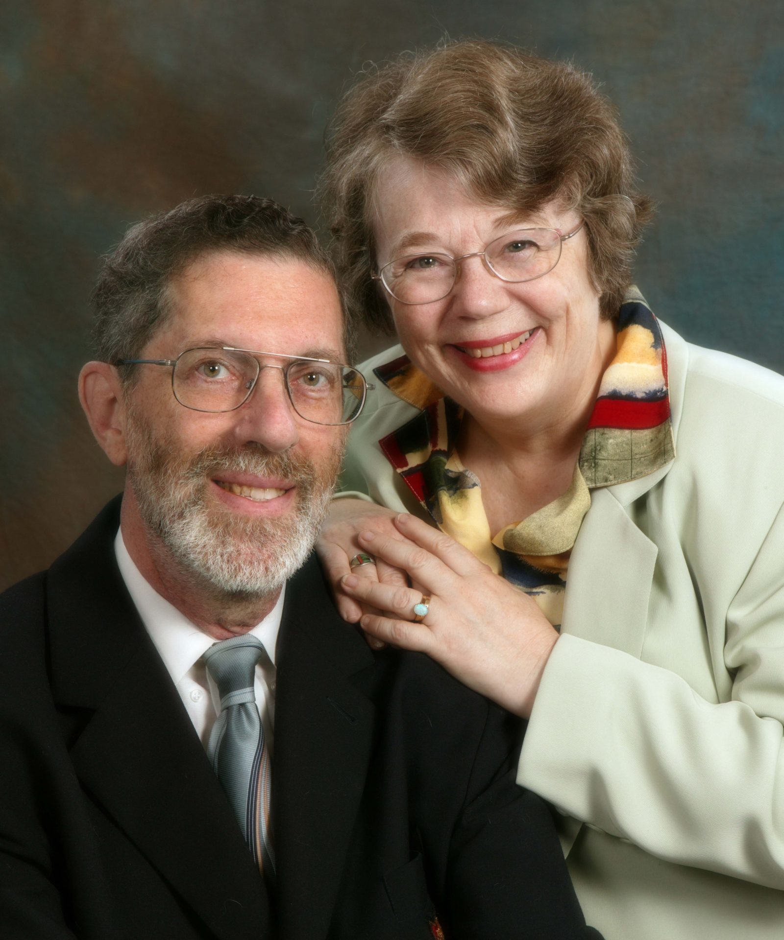 A man and a woman pose together in front of a beige backdrop.