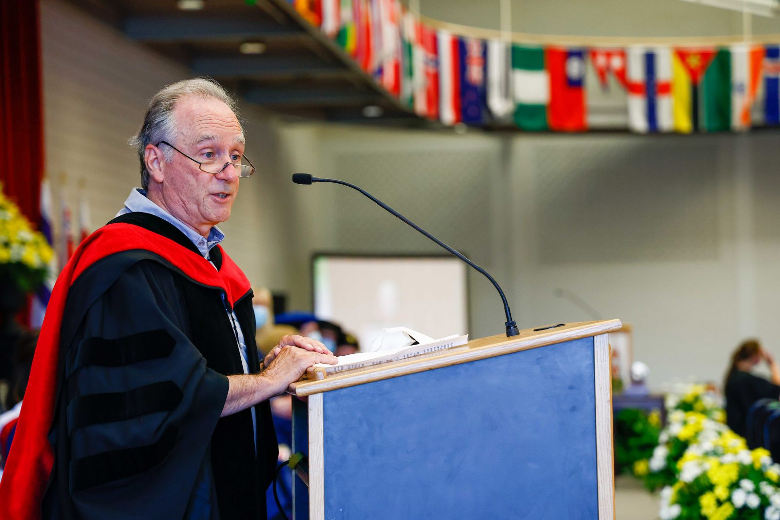 A man in a Convocation gown stands speaking at a podium.