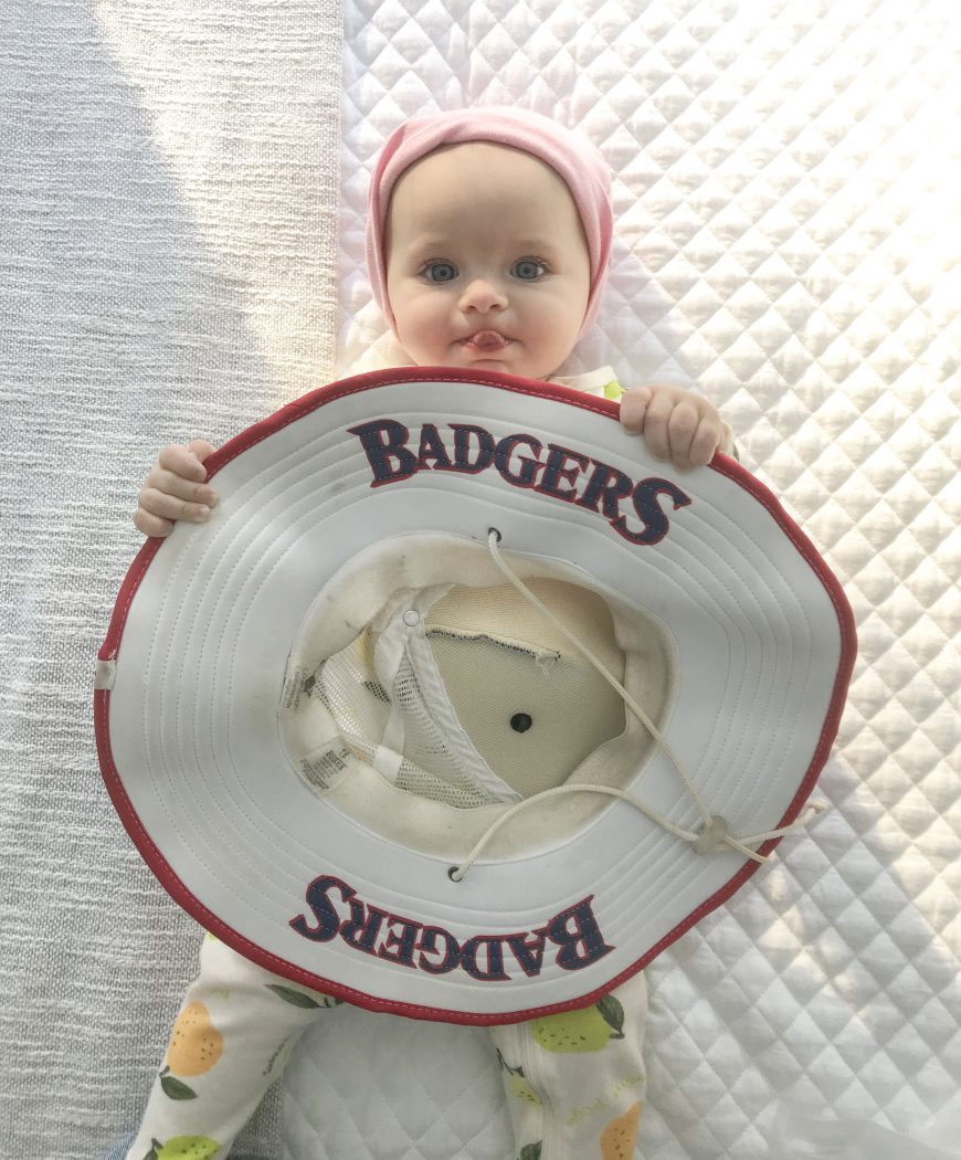 A baby girl holds a Brock University brimmed hat that says Badgers on it.