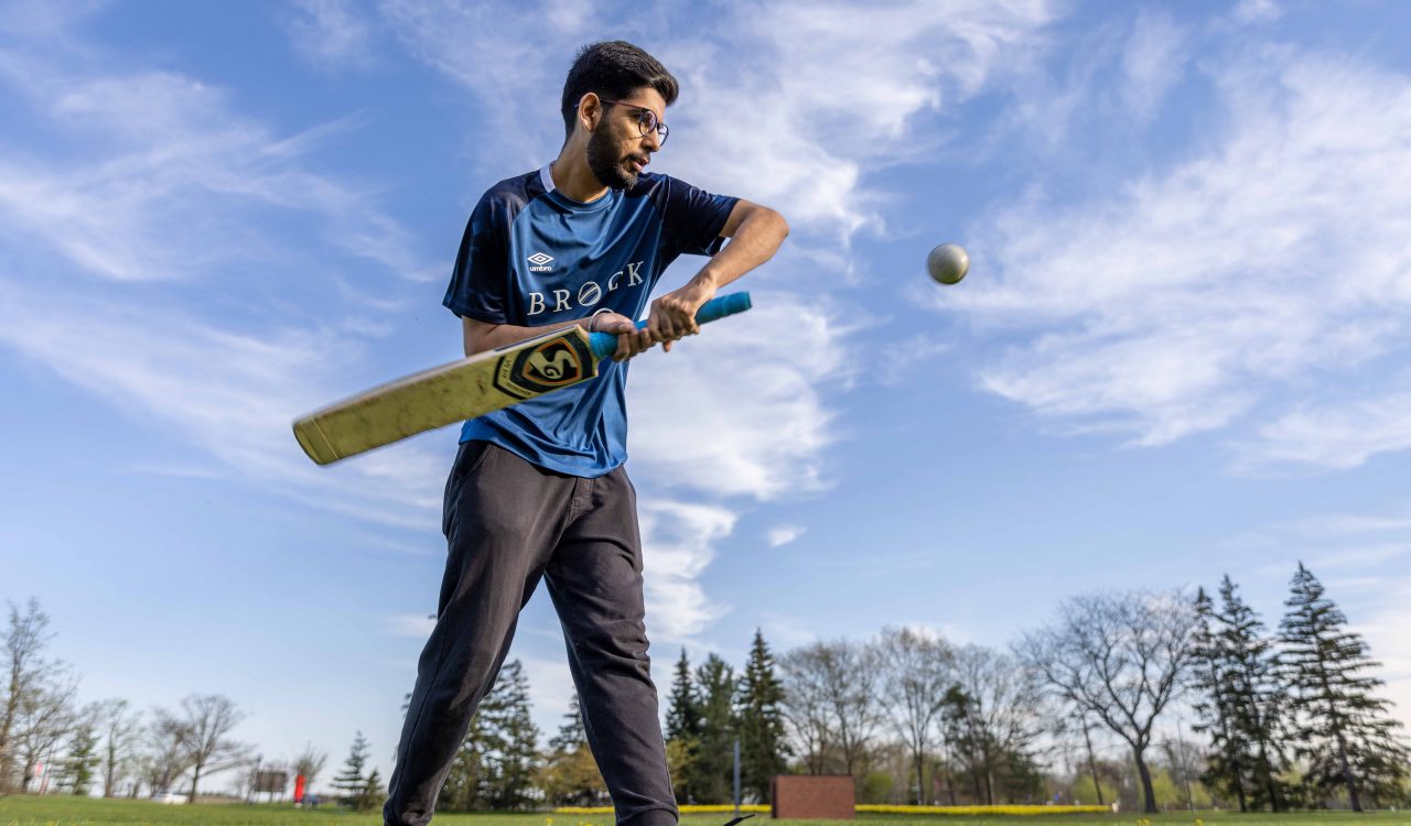 A cricket player swings a bat in an open field.