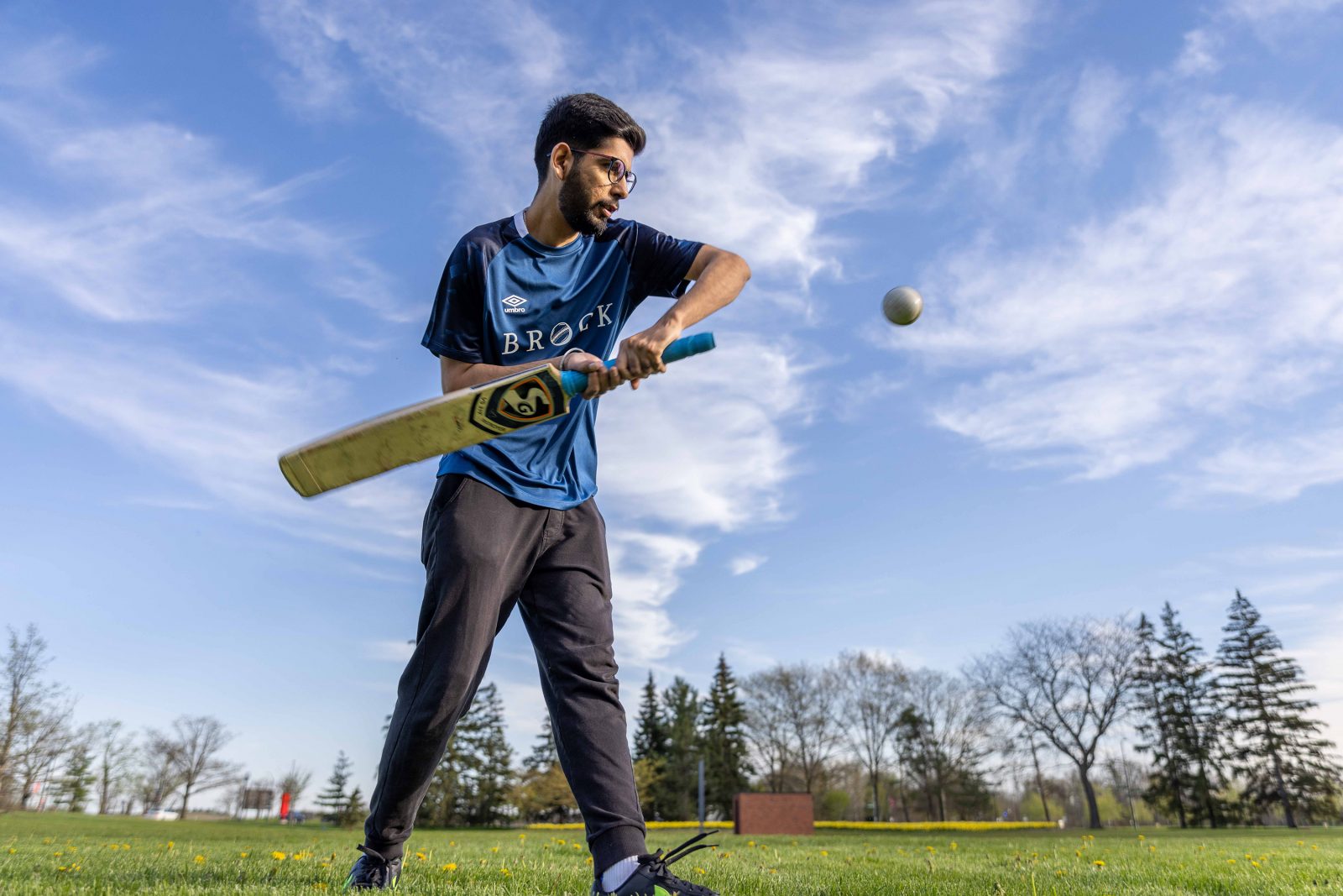 A cricket player swings a bat in an open field.