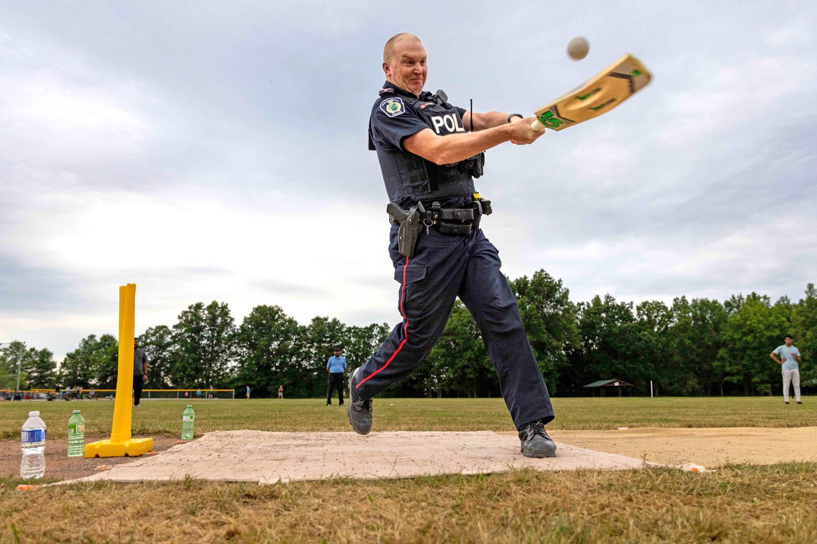 A police officer swings a cricket bat in a field.