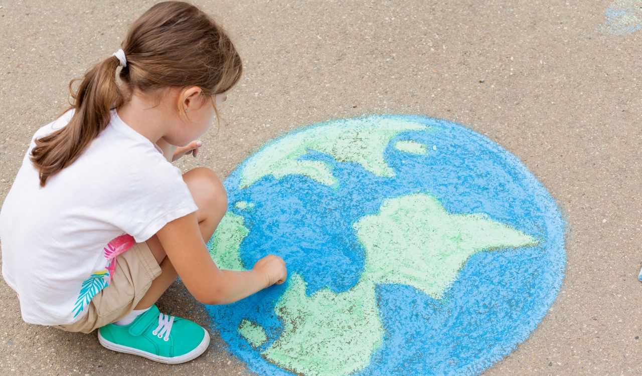A young girl crouches over a chalk drawing of Earth on concrete.