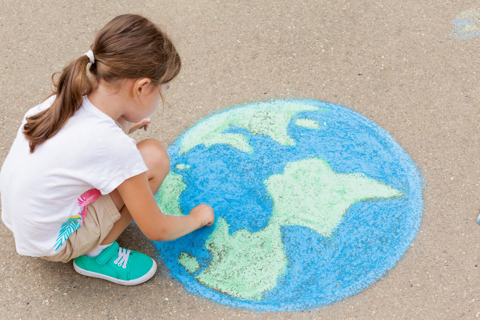 A young girl crouches over a chalk drawing of Earth on concrete.