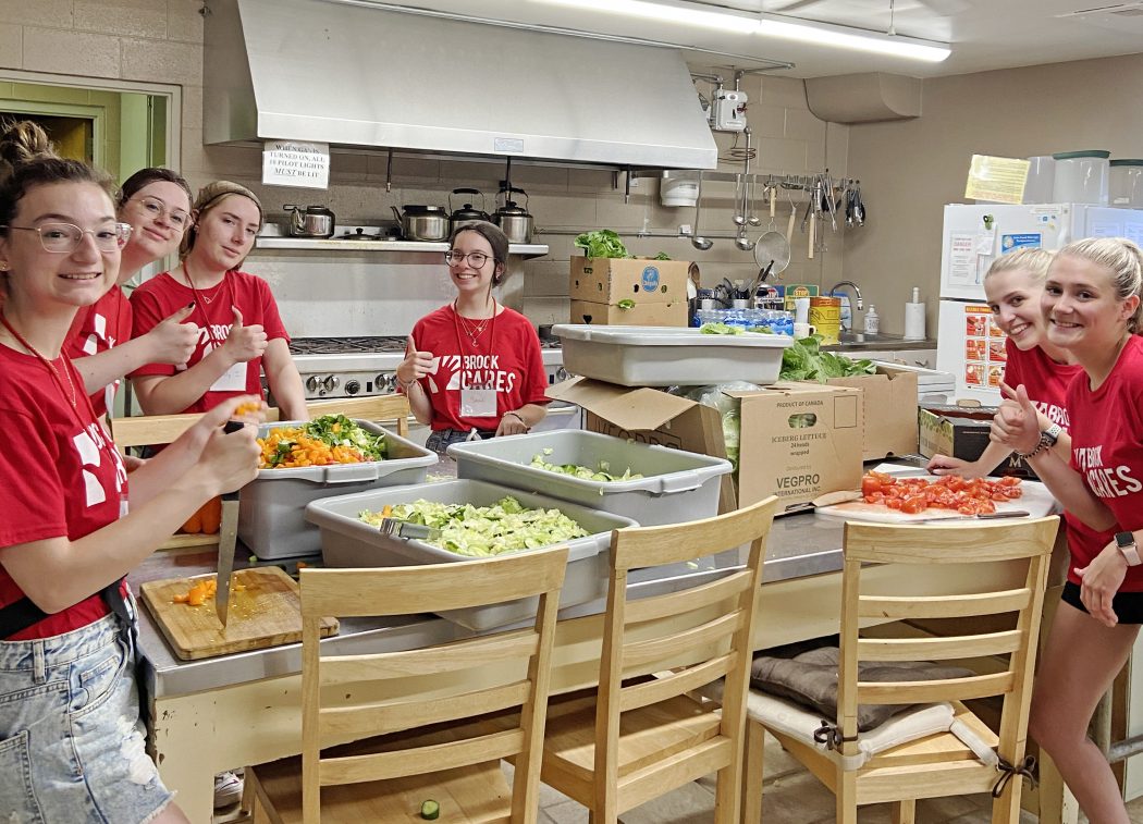 Six women in red shirts stand in a kitchen while preparing food.