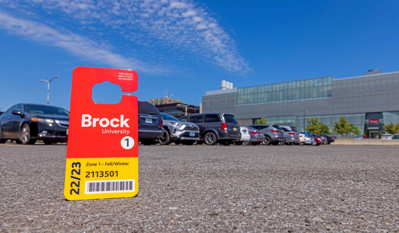 A parking pass sits on the asphalt of a university campus parking lot.