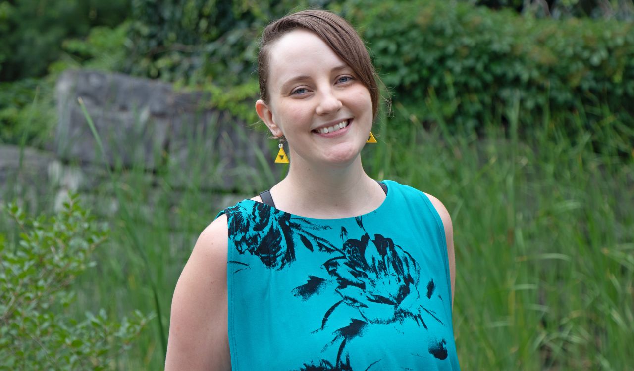 A portrait photo of Assistant Professor Sarah Stang in a sleeveless teal shirt with a large black flower design.