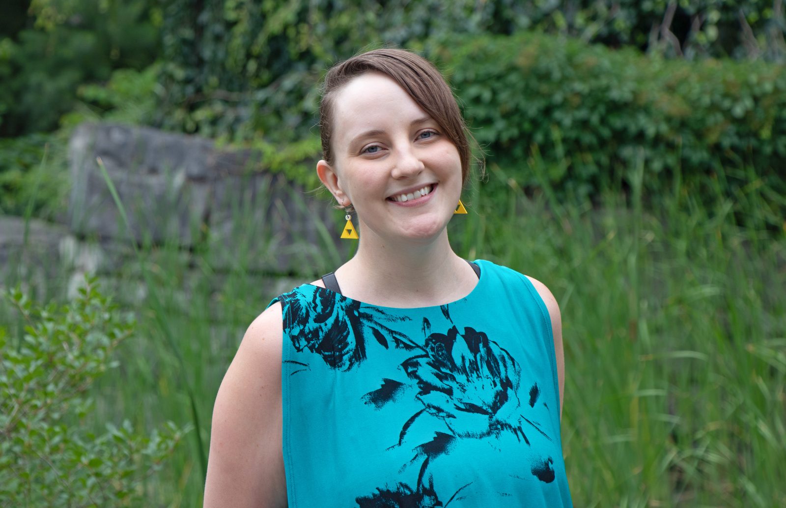 A portrait photo of Assistant Professor Sarah Stang in a sleeveless teal shirt with a large black flower design.