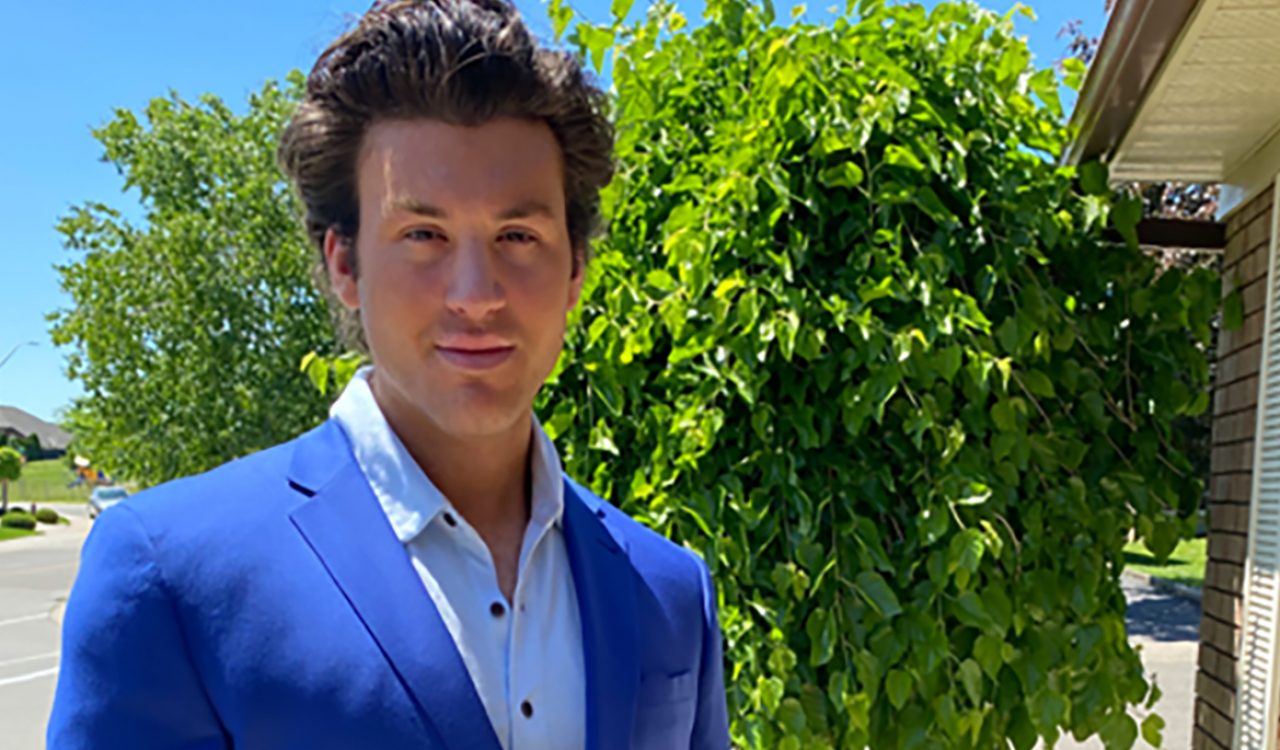 Steven Kottaras, a man in a blue suit, stands in front of a green tree.