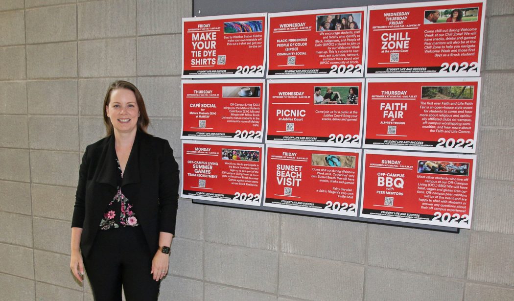 A woman in a black suit stands next to a bulletin board with a series of events listed on it.