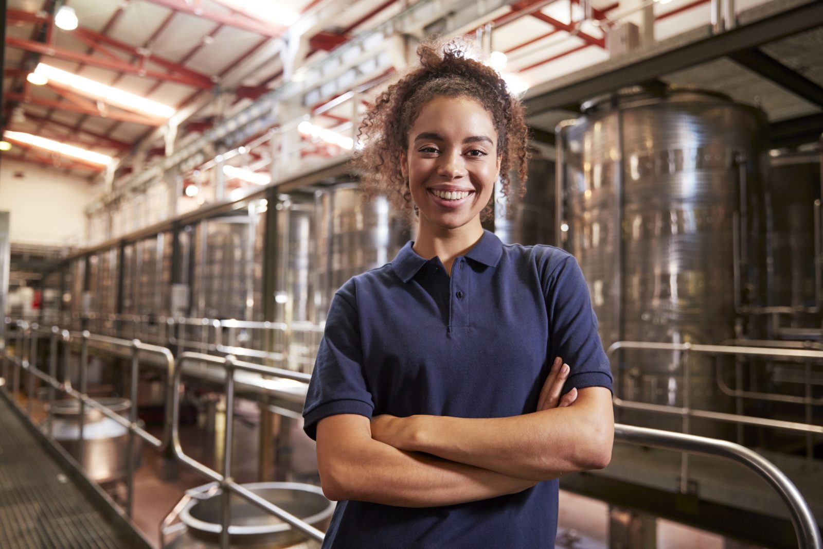 A portrait of a woman standing in front of large metal wine vats.